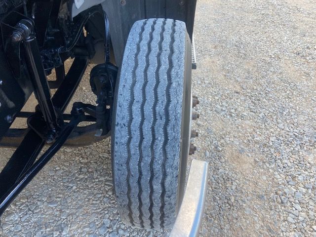 Truck front wheel and suspension area showing dual rear axle configuration with treaded tire on the front drive axle.