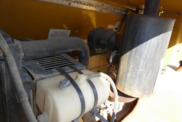 Trucking equipment engine bay showing coolant reservoir with strap, hoses, and large cylindrical component.