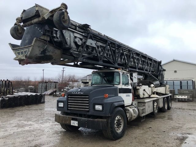 Mack RD688S concrete pump truck with long boom folded overhead, blue cab, white mixer area, front grille and headlights visible.