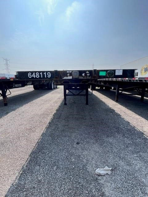 Manac steel flatbed trailer undercarriage view showing frame and landing gear with serial 648119 on the neck.