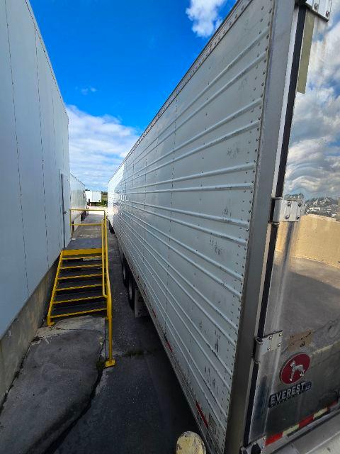 Great Dane SS reefer trailer side view showing aluminum ribbed walls and rear doors with hinges; blue sky background.