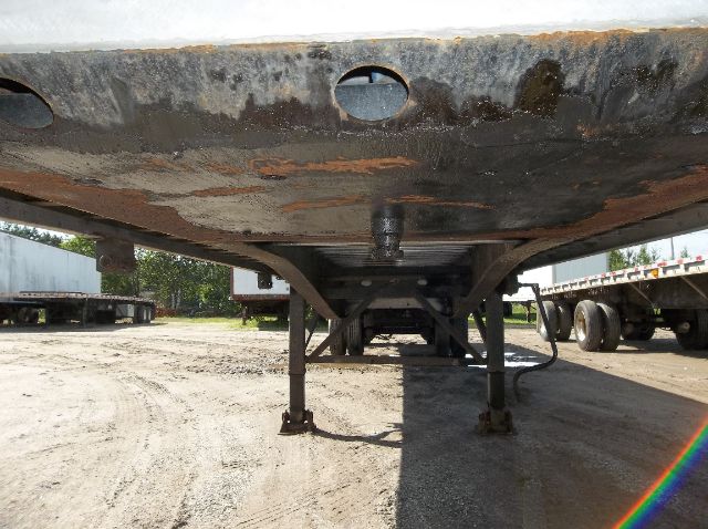 Underbelly of a flatbed trailer showing support legs and rusted frame.