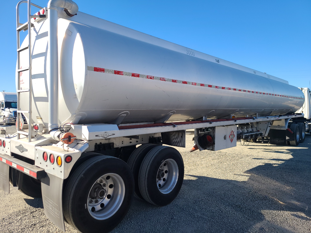 Beall semi trailer showing cylindrical tanker with rear wheels and ladder, white with red/white reflective stripe and safety equipment.