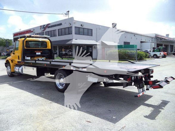 Tow truck flatbed (2019 International DURASTAR 4300) with yellow cab and long flat bed, rear view shows towing equipment and hooks.