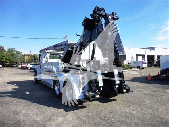 Freightliner Business Class M2 106 tow truck with a hydraulic boom and truck-mounted crane, side view showing white cab and black lifting arm.
