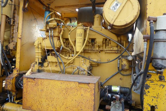Caterpillar engine bay in a 1978 16G grader showing CAT diesel engine with hoses, wiring, and a yellow reservoir; heavy equipment cab area partially visible.