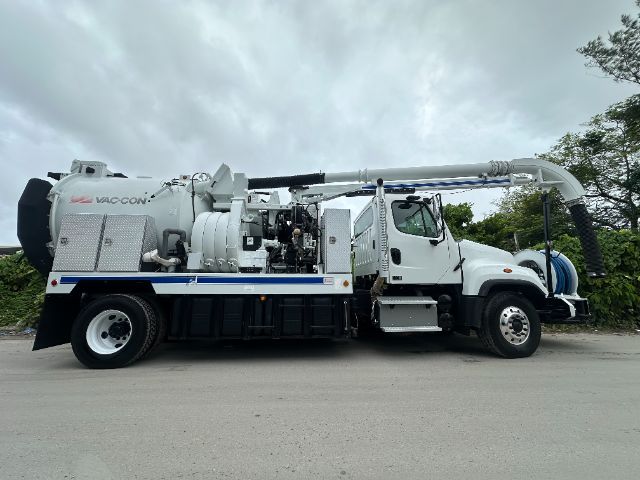 Side view of a white 2014 Freightliner 114SD vacuum truck with mounted vacuum system and hose reel.
