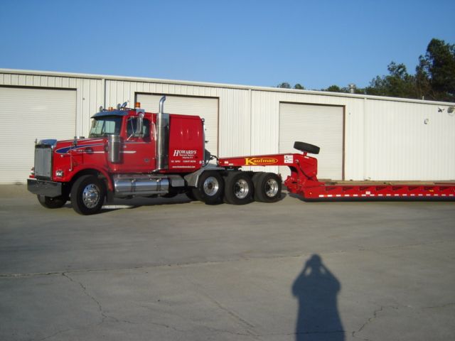 2007 Western Star 4900fa conventional sleeper truck with a red tow/flatbed trailer attached, parked in front of a white building.
