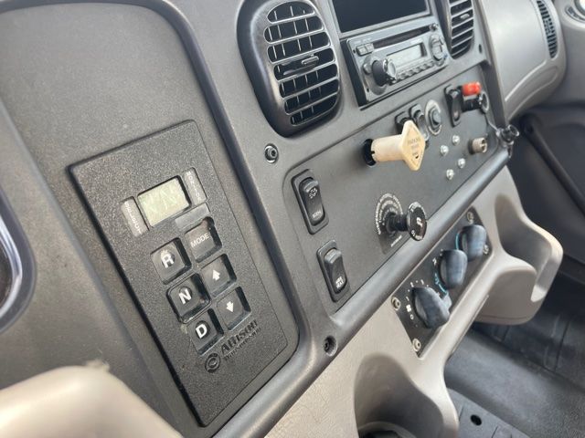 Dashboard controls in a Freightliner M2 cab showing gear selector, climate dials, and radio area.