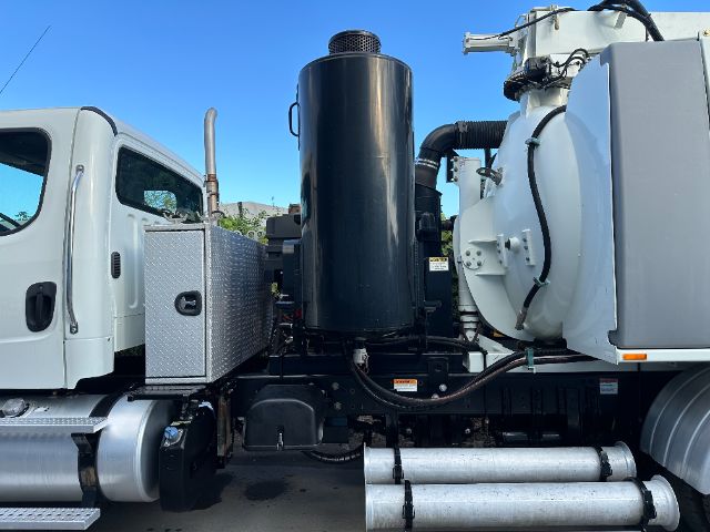 Truck side view showing large cylindrical exhaust/air filter housing and white tanker body with hoses. Visible components include a shiny metal toolbox, steps, and hydraulic lines.