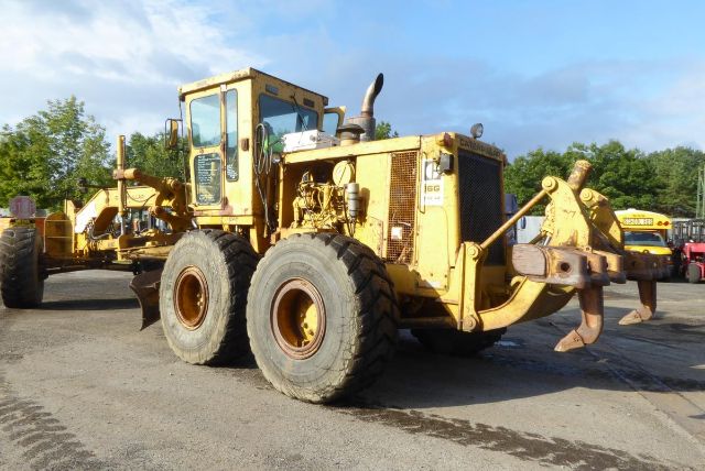 Caterpillar 16G motor grader in-service with front blade and rear ripper attachment, beige-yellow paint, large off-road tires.