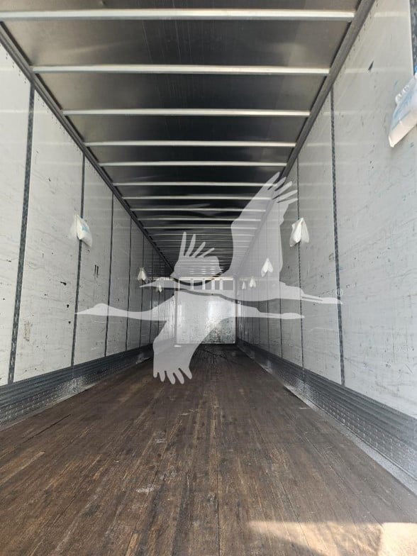 Trailer interior showing empty cargo area with wooden floor and side walls; long tunnel-like trailer with overhead rails and small white fixtures.