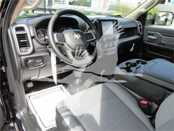 Ram pickup interior showing steering wheel with controls, center console, touchscreen display, and driver's seat. Visible text includes none clearly readable beyond generic dashboard elements.