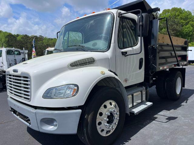 Freightliner M2 106 dump truck side view showing white cab and dump bed with dual rear wheels and chrome wheel covers.