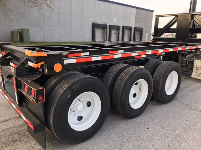 Trailer wheels and frame of a 2003 Wabash tipper in blue/black with white rims and reflective orange/white tape.