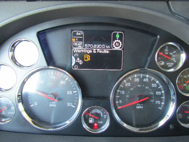 Dashboard of a Kenworth truck showing gauges including RPM, speedometer, fuel gauge, and a central digital display with warnings and Faults. The display reads temperature 64F, 570,830.0 miles, and various warning icons.
