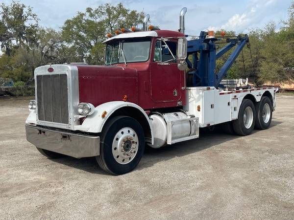 Peterbilt 359 tow truck with maroon cab and white front, large chrome grille, white fenders, and a blue boom present on a blacktop lot.
