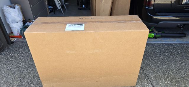 Box on driveway in front of a vehicle with a label on top; no other parts visible.