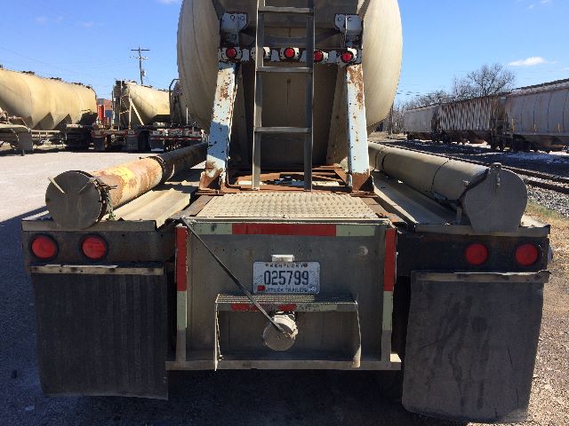 Rear view of a pneumatic dry bulk trailer with visible mudguards, taillights, and a license plate; spare tubes and support structure on the bed.