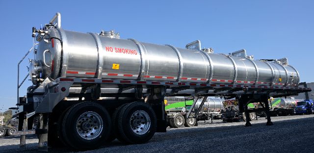 Vacuum trailer mounted on a multi-axle tractor, aluminum cylindrical tank with no smoking label, equipment markers, and support legs extended.