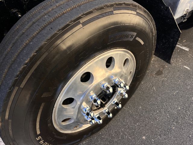 Wheel showing polished steel rim with chrome lug nuts and black tire. Partial fender and truck body nearby.