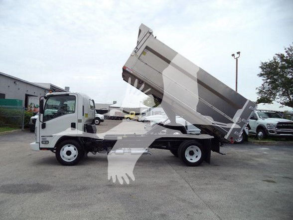 Isuzu NPR HD dump truck in a dealership lot with bed raised for dumping.