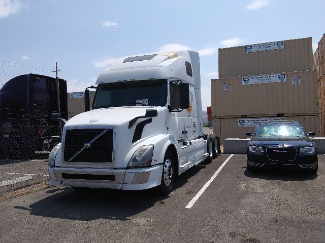 Volvo 670 semi-truck in a parking lot with stacked shipping crates and a dark car beside it.