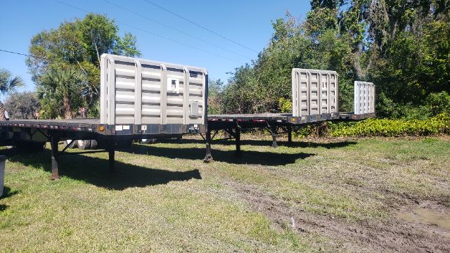 Great Dane flatbed trailer with three modular silos or headboards on a long extendable flatbed, set on grassy lot under clear sky.