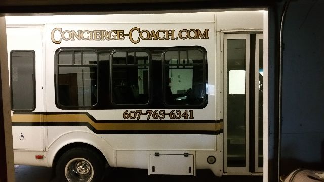 Bus exterior with Concierge-Coach.com branding and phone number along the side, rear window and door visible.