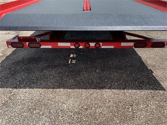 Flatbed trailer rear showing lighting/reflective tape and bumper with dual taillights; black undercarriage visible.