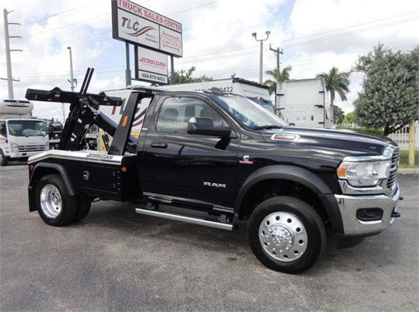 Ram 4500 tow truck with flatbed wrecker equipment, black cab, chrome front grille, large dual rear wheels, towing hardware in bed, showroom lot.