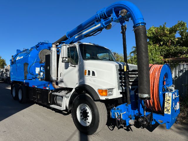 Sterling L7500 vacuum truck with white cab and blue vacuum body, large hose reel and exhaust stack visible.