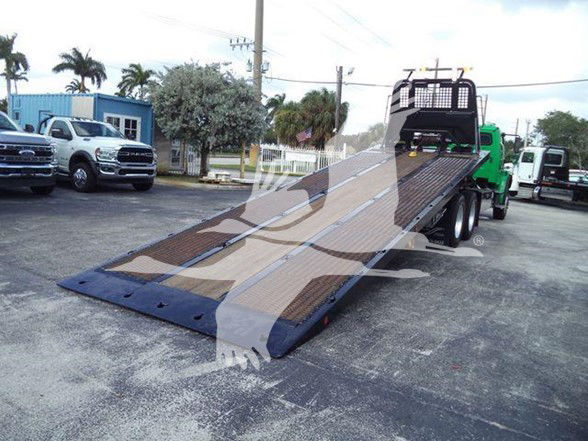 Flatbed tow truck with a long ramp, Freightliner business class M2 106 style. Visible are a green cab and brown wooden ramp surface with black end plates.