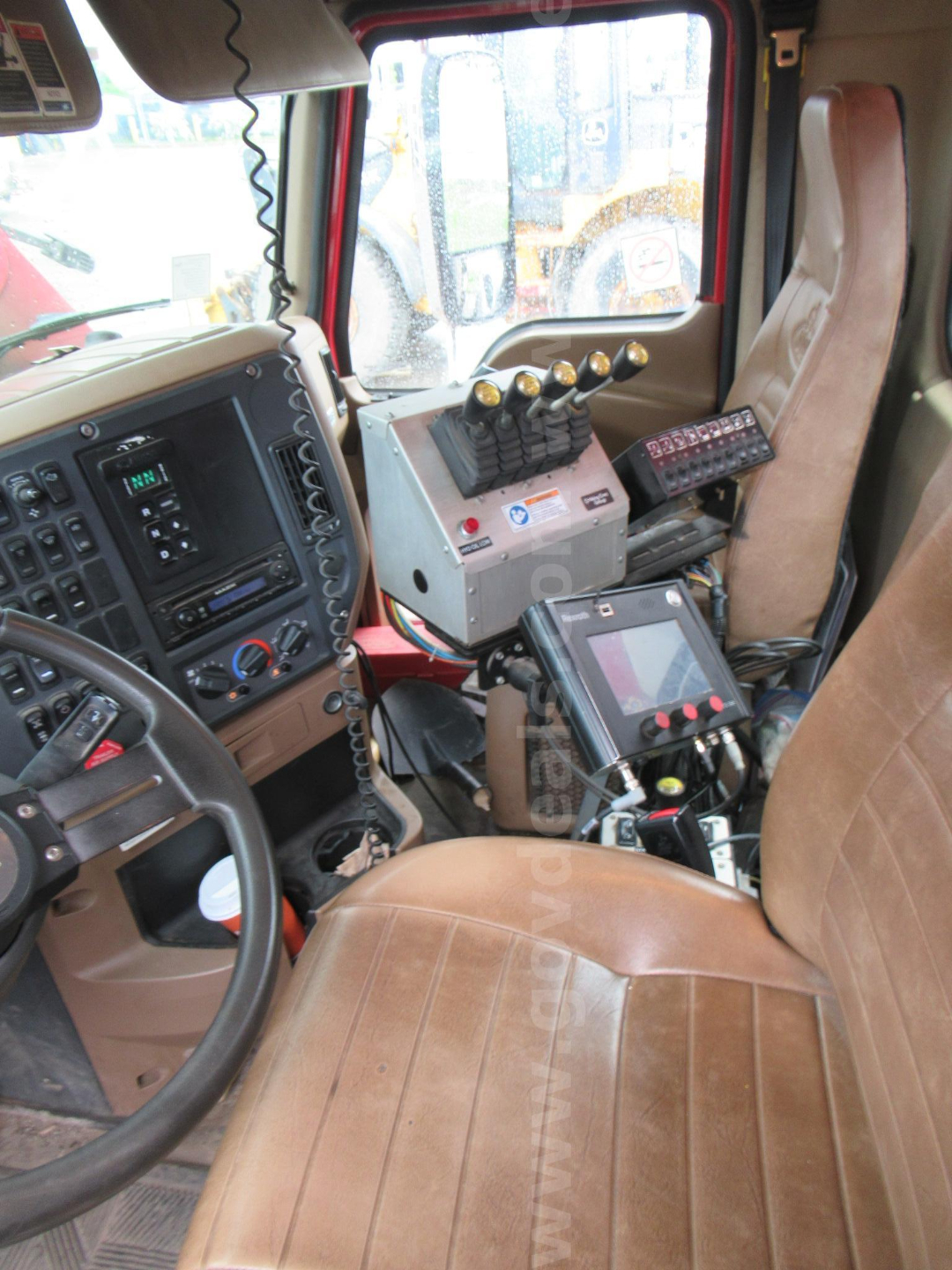 Cab interior of a Mack GU713 showing steering wheel, dashboard, control module with levers, and mounted electronic display panel.