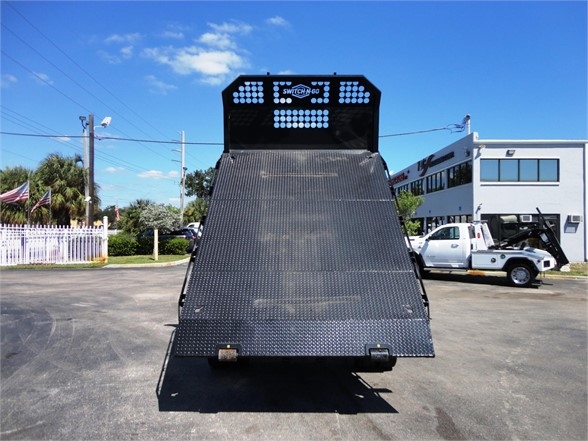 Ram 5500 HD truck bed with a flatbed/dropped ramp in a hooklift configuration, back view, metal diamond plate surface, rear lights and headboard visible.