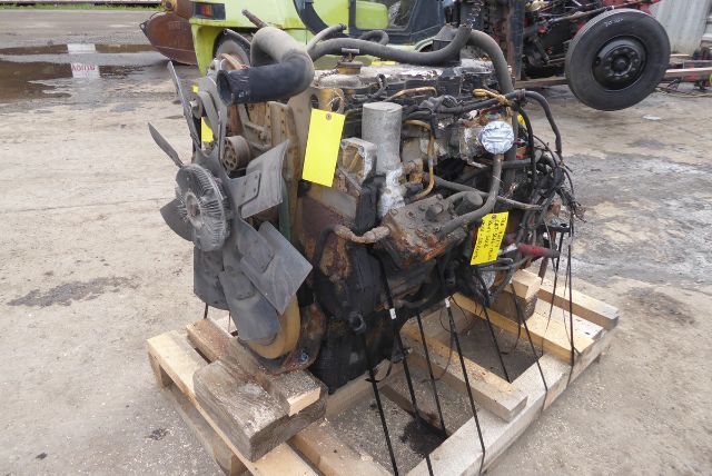 Truck engine block with attached hoses, belts, and a large cooling fan mounted on a wooden pallet. Various yellow tags and labels are attached to components.