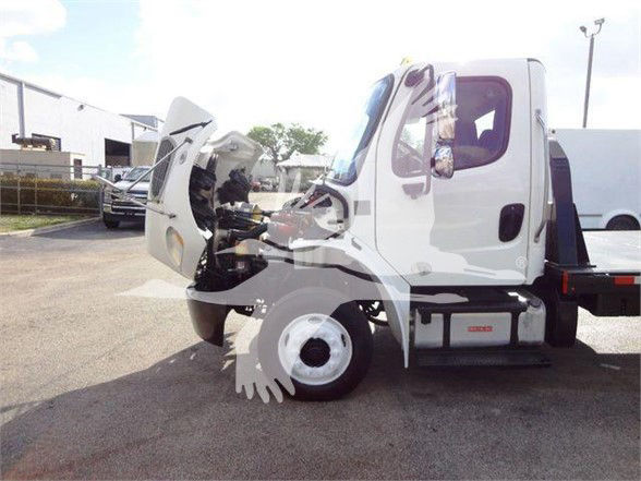 Truck cab interior visible with front hood open, Freightliner M2 106 flatbed truck, white exterior, side steps and engine area exposed.