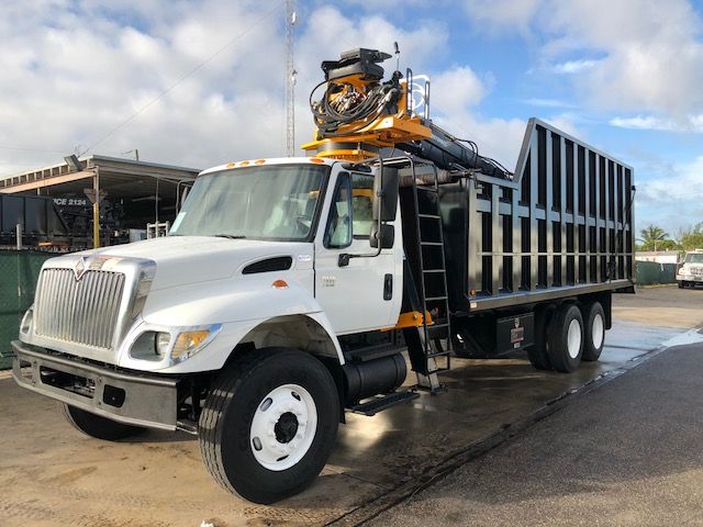 International dump truck with grapple crane mounted on cab showing white cab, black dump body, and yellow crane. No visible text legible on components.