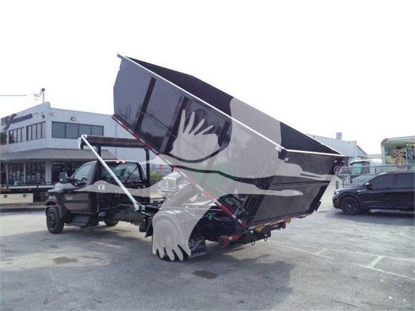 Truck with large dump bed raised, showing hydraulic lift and rear wheels. Silverado 6500HD in background; no legible labels readable.