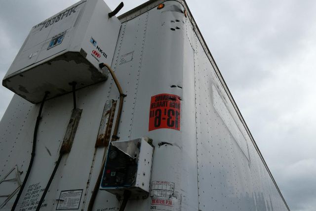 Rear corner of a white trailer with a climate control unit mounted on top left; visible labels include a red '3-8-9' warning sticker and a small electrical box with cables; riveted aluminum panels.