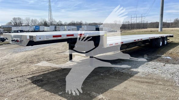 Transcraft drop deck trailer with long flatbed, side rails, and triple axles showing VIN and stock number on the listing.
