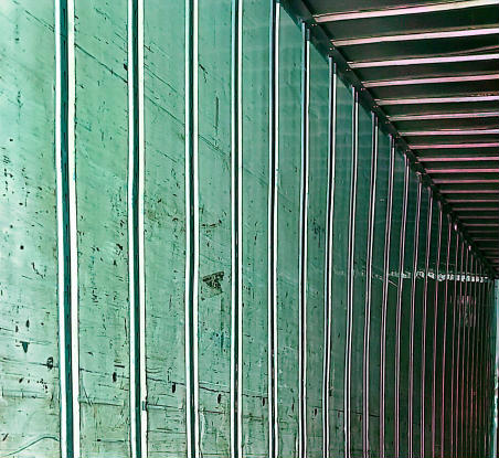 Trailer interior wall with vertical metal studs and green wall panels.