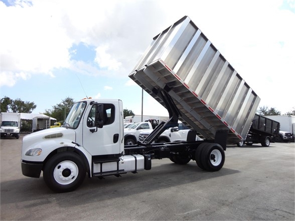 Truck cab with a raised metal dumping bed in a tipping position, Freightliner chassis, diesel engine, chassis and wheels visible.