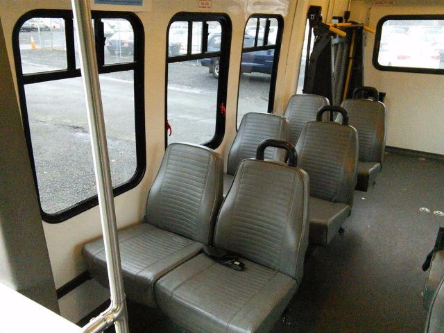 Interior of a 2009 Ford E-450 bus showing gray vinyl seats arranged in rows with windows along the sides.