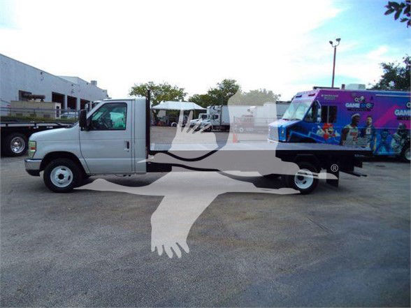 Flatbed truck in a dealership lot showing a white Ford E-Series cab in front and a flatbed with a purple/blue bus on the rear. Visible text on the image includes VIN and stock info likely overlay and not readable on the vehicle itself.