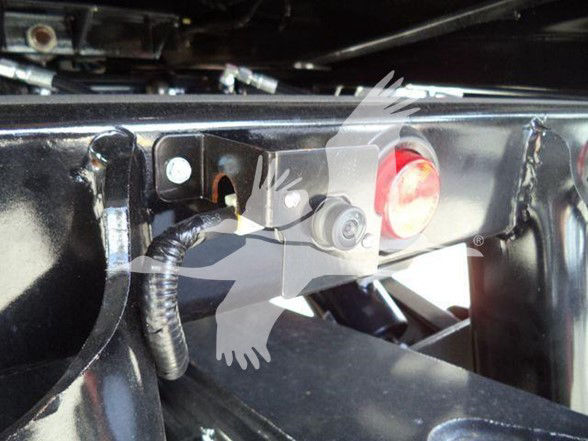 Truck hitch area with a red circular rear bumper sensor/adapter and wiring, metal brackets and a small black connector.