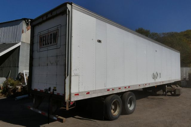 Fruehauf FBHLP 9-1.5 H2 trailer with dual rear axles, white exterior, yellow sign on back, parked in a lot.
