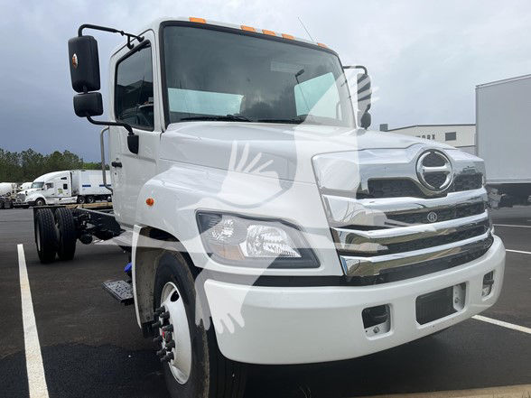 Front view of a white 2026 Hino L6 cab and chassis truck showing front grille, headlights, and side mirror. The image includes a faint watermark logo overlay.