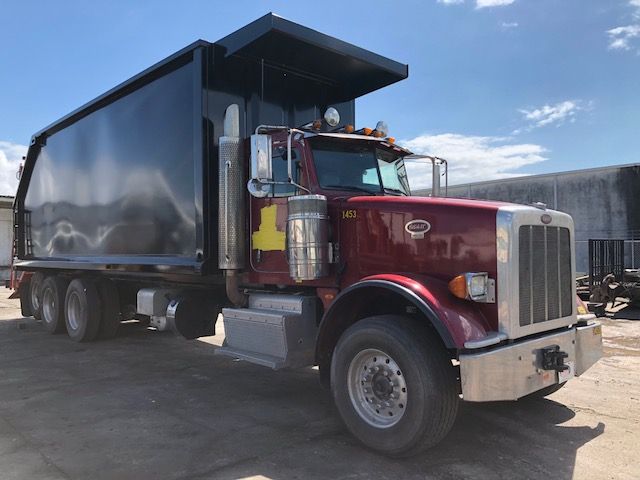 Peterbilt 388 dump truck in a maroon cab with a black dump body, chrome mirrors, and large vertical exhaust stacks; number 1453 on door.