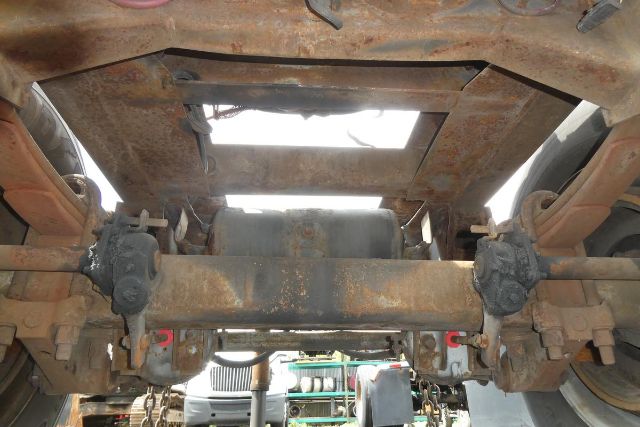 Dolly trailer underside showing suspension axle hangers and leaf springs with rust, frame crossmember, and center oil/air tank with brackets.